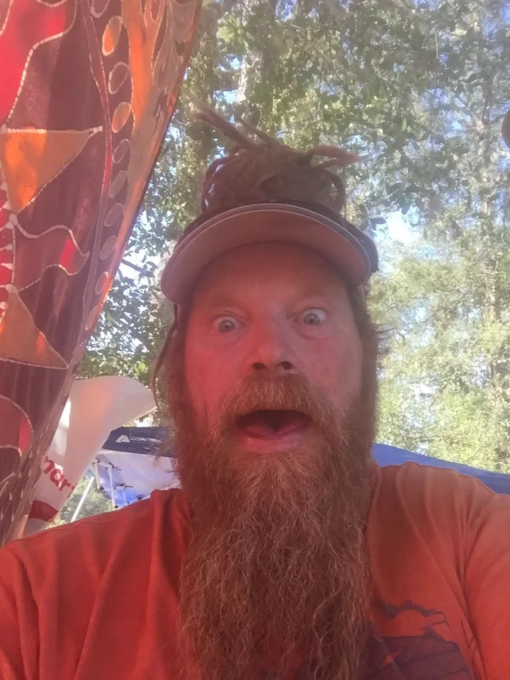 Rusty outdoors under a hanging batik, mouth open in mock surprise, trees overhead.